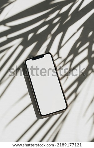 Smart phone with copy space mock up screen on white background with palm leaves shadow. Flat lay, top view blog template.