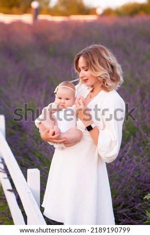Happy mother with pretty daughter on lavender background. Beautiful woman and cute baby sitting in meadow field. Family holiday in summer day.