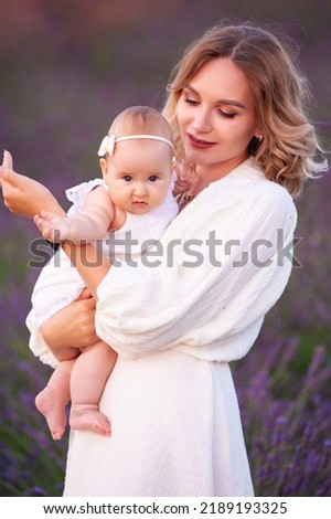Happy mother with pretty daughter on lavender background. Beautiful woman and cute baby playing in meadow field. Family holiday in summer day.