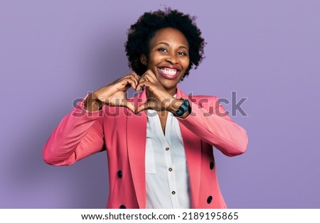 African american woman with afro hair wearing business jacket smiling in love doing heart symbol shape with hands. romantic concept. 