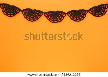 Black crochet spider web on orange background with copy space for text. Halloween autumn decoration scary creepy horror concept. Idea for banner, postcard, poster. Spooky Cobweb. Flatlay, mock up