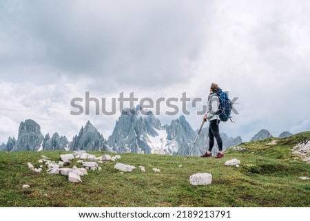 Woman trekker with backpack and trekking poles on the hill enjoying picturesque Dolomite Alps view near Tre Cime di Lavaredo formation in South Tyrol, Italy. Active people and mountain concept.  Royalty-Free Stock Photo #2189213791
