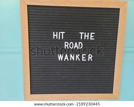 A sign hanging on a door saying hit the road wanker. The felt sign has removable letters than can be moved around to make whatever words or saying one wants. 