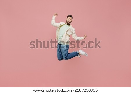 Full body young smiling happy fun man 20s wearing trendy jacket shirt jump high do winner gesture clench fist isolated on plain pastel light pink background studio portrait. People lifestyle concept Royalty-Free Stock Photo #2189238955