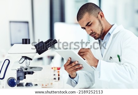 Serious male scientist working on a tablet reviewing an online phd publication in a lab. Laboratory worker updating health data for a science journal. Medical professional document clinical trial Royalty-Free Stock Photo #2189252113