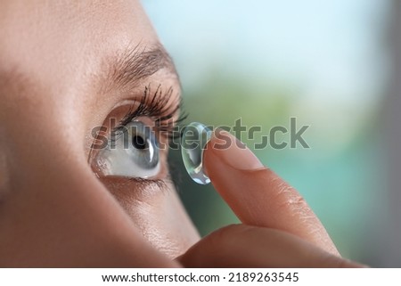 Young woman putting contact lens in her eye on blurred background, closeup Royalty-Free Stock Photo #2189263545