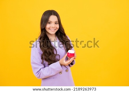 Teen girl hold facial cleaner for skin wash, cleansing scrub. Child presenting cosmetic product for teen. Kid use face cream isolated on yellow background.