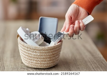 digital detox and technology concept - close up of hand holding smart watch and different gadgets in wicker basket on table at home Royalty-Free Stock Photo #2189264167