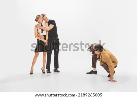 Portrait of man in yellow retro jacket taking photo with vintage camera of beautiful couple isolated over white studio background. Concept of retro fashion, style, youth culture, emotions, beauty, ad