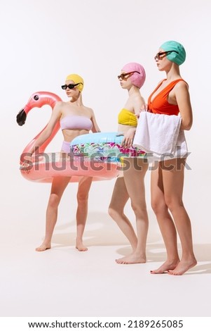 Portrait of young women in swimming suit, cap and sunglasses posing with swimming circle isolated over grey studio background. Beach party Concept of beauty, fashion, vintage style, summertime, party.