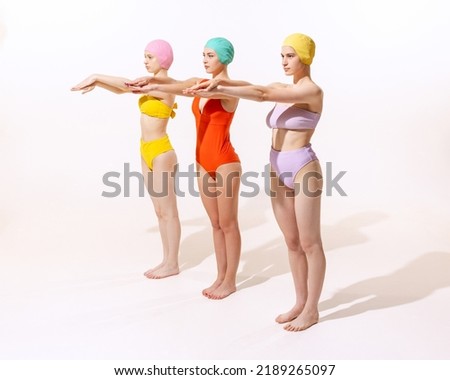 Portrait of three young women in vintage retro swimming suits posing isolated over grey background. Swimming lesson. Concept of beauty, fashion, vintage style, summertime, party. Copy space for ad