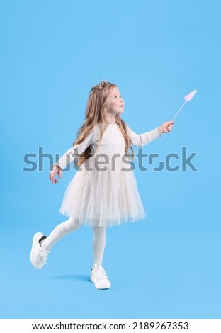 Cute girl in fairy dress with diadem and magic wand on light blue background. Little princess Royalty-Free Stock Photo #2189267353