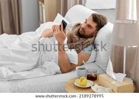 health, illness and people concept - sick man with smartphone in bed at home Royalty-Free Stock Photo #2189278995