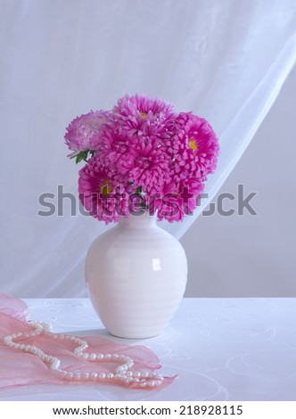 Photo bouquet of pink asters in a white vase with a pink scarf and white pearls on a white background curtain