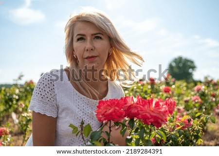 young pretty fair-haired girl near a rose bush looks to the side, nature, travel, rest