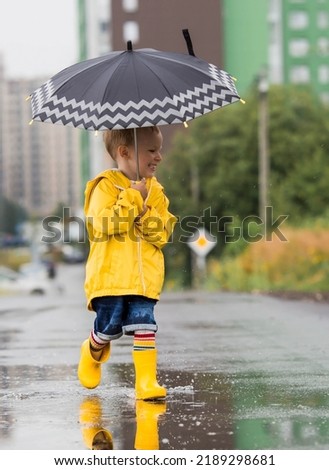 A small child in rainbow socks, yellow rubber boots and a jacket runs through puddles, has fun and plays after the rain. A picture of summer and autumn holidays. A child under an umbrella.