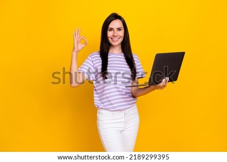 Photo of funny positive lady show okey symbol offer quality modern device gadget netbook empty space isolated on yellow color background