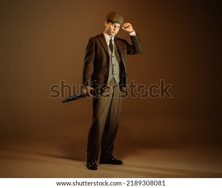 Retro style portrait of young man in image of english gangster, businessman wearing suit and cap standing isolated over dark vintage background. Concept of business, personality, emotions, fashion Royalty-Free Stock Photo #2189308081
