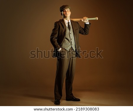 Retro style portrait of young man in image of english gangster, businessman wearing suit and cap standing isolated over dark vintage background. Concept of business, personality, emotions, fashion Royalty-Free Stock Photo #2189308083
