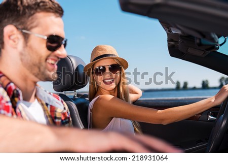 Having freedom to go anywhere. Beautiful young couple enjoying road trip in their convertible while beautiful woman looking at her boyfriend and smiling