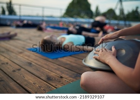 Group of young people practicing yoga lesson lying in Dead Body or Corpse pose, Shavasana exercise. Hands with drum on a foreground Royalty-Free Stock Photo #2189329107