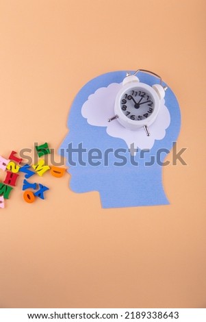 Alarm clock in humans head ans small colorful letters running out his mouth. Vertical photo on loght pink background