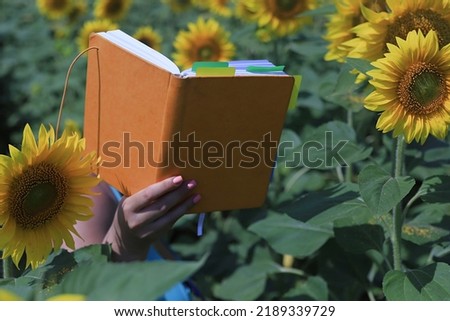 notebook in an orange cover against the background of a field of sunflowers.