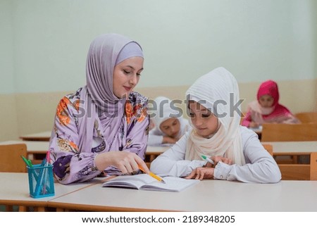 Female hijab Muslim teacher helps school child to finish the lesson in the classroom.	