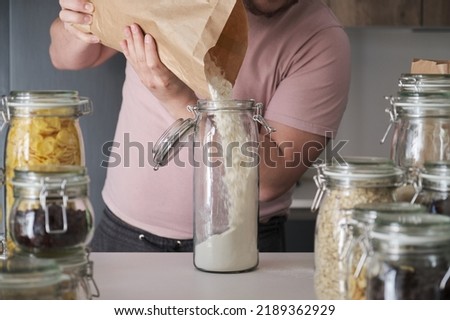 Unrecognizable latin man filling up a jar with wheat flour from a paper bag. Food in bulk delivery. Royalty-Free Stock Photo #2189362929