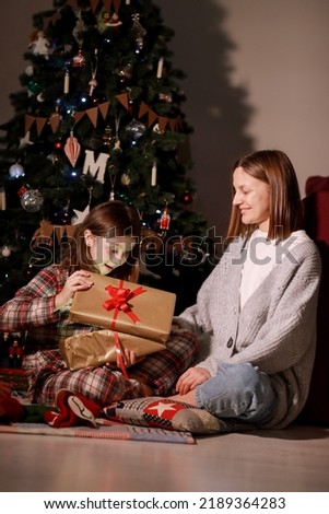 young mother and daughter open Christmas Lighting Present Gift Box front of Xmas Tree. Happy Mom with kid girl in Magic Night. Family merry christmas and new year holiday concept. High quality photo.