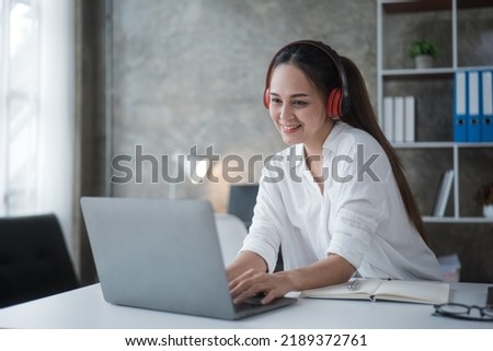 Happy woman is listening music via headset while working or study on laptop at home or office space.