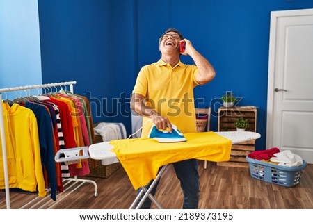 Middle age man talking on the smartphone ironing clothes at laundry room