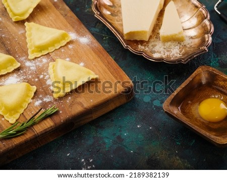 Italian homemade ravioli on a wooden cutting board, ingredients on a dark marble background. Cooking homemade ravioli with meat. Italian food. Advertising, banner.