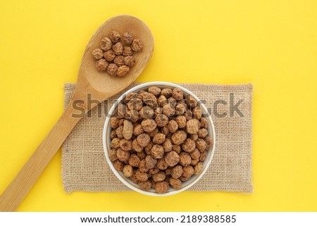 Chufa, tigernut, earth almond on white ceramic bowl and eco canvas bag near wooden spoon on yellow background. Healthy vegan food concept. Tiger nut for flour, oil, milk, traditional drink horchata
