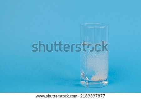 An effervescent tablet that dissolves and fizzes in a glass of water on a blue background. Headache treatment.