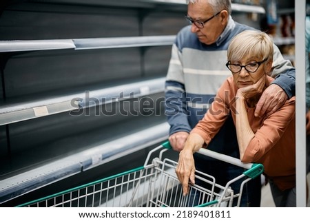 Senior woman and her husband feeling concerned about empty shelves and shortage of food in supermarket. Royalty-Free Stock Photo #2189401811