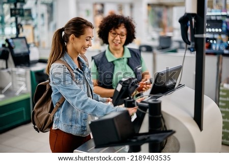 Happy supermarket customer using self-service till with help of a manager. Royalty-Free Stock Photo #2189403535