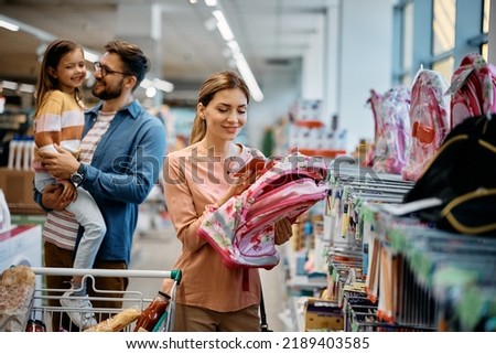 Happy family buying backpack and school supplies in a store. Focus is on mother looking at price on a backpack.