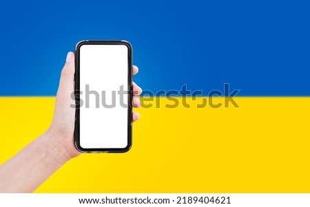 Close-up of male hand holding smartphone with blank on screen, on background of blurred flag of Ukraine.