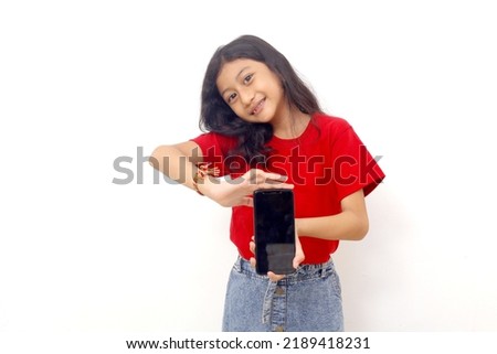 Happy asian little girl standing while showing a blank cell phone display. Isolated on white