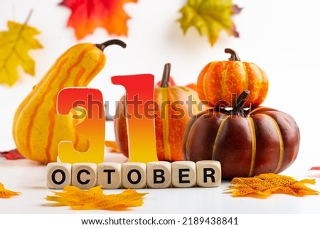 Colorful pumpkins and bright autumn leaves on a white background. The inscription OCTOBER 31 is assembled from bone cubes.