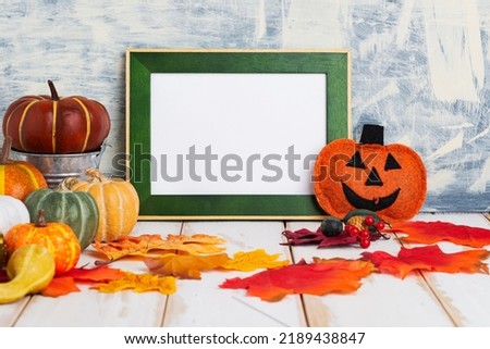 Halloween holiday concept with empty green frame and pumpkins on a light table against a light wall. copy space,