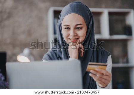 Portrait of a Muslim businesswoman shopping on her credit card phone. smiling arab woman taking notes and work on laptop