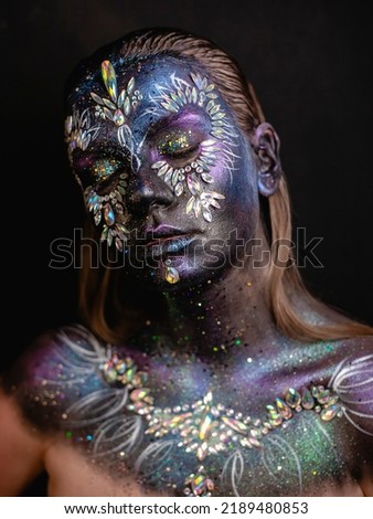 Creative makeup girl with rhinestones and feathers on a dark background