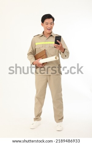 Full length body photo of an Asian young handsome construction worker, holding blue print, in working uniform, isolated on white background