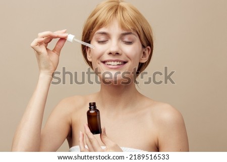 A nice woman in a towel with white clean well-groomed skin, short red hair on a beige background with a new serum takes care of her face after a bath in the morning.Close-up photo. Horizontal studio
