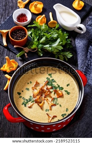 Kanttarellikeitto, Finnish Chanterelle Soup in red pot on dark wooden table with ingredients on background, vertical view from above,