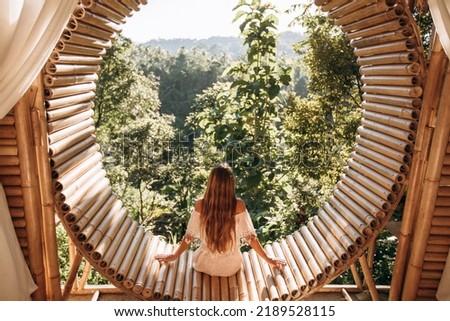 Attractive girl enjoys a beautiful view while sitting on a bamboo terrace overlooking the jungle in the mountains. Bamboo house in the mountains. Ecological housing Royalty-Free Stock Photo #2189528115