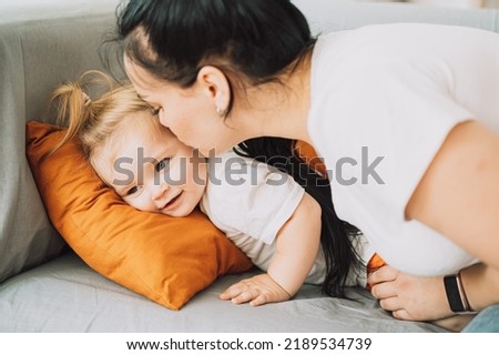 Little girl lying on the sofa and mom kissing her.