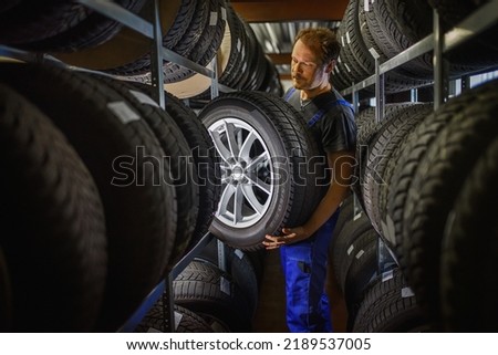 Hardworking experienced worker holding tire and he wants to change it In the tire store. Selective focus on tire. Royalty-Free Stock Photo #2189537005